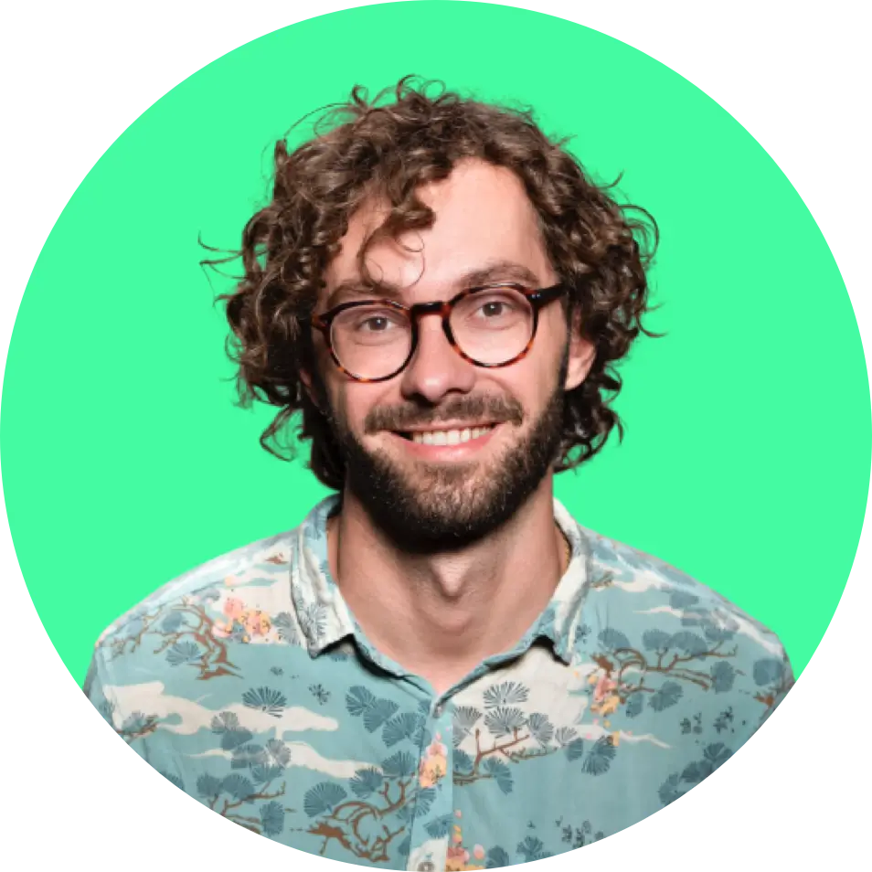 ortrait of the company founder, 
      a smiling man with curly hair, glasses, and a floral shirt on a green background.